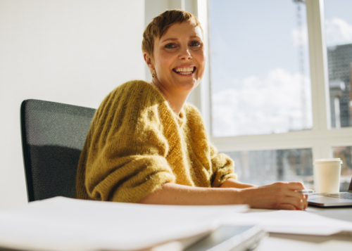 Smiling woman in an office setting, representing the EndoAware Workplace Accreditation Programme by Endometriosis Australia.